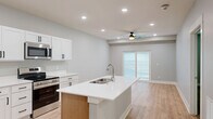 Located at 8801 Mohave Dr in Lincoln, Nebraska, this thoughtfully designed one-bedroom, one-bathroom unit offers a clean, contemporary aesthetic throughout its efficiently organized single floor. The open-concept kitchen and living area serves as the heart of the home, anchored by a central island with a white quartz countertop and undermount sink. Crisp white shaker cabinets with matte black hardware complement a full suite of stainless steel appliances, including a French door refrigerator, electric range, and over-the-range microwave. Light hardwood-style flooring flows throughout the main living areas, enhancing the bright, airy feel. The living area benefits from recessed lighting, a ceiling fan, and sliding glass doors that open to a private balcony, inviting natural light and outdoor views. The spacious primary bedroom features plush carpet, recessed lighting, and access to generous closet storage with built-in shelving. A dedicated laundry closet with a full-size washer and dryer adds everyday convenience. Neutral gray tones on the walls throughout create a calm, cohesive palette, making this well-appointed unit an inviting and functional place to call home.