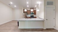 This single-floor unit in Asheville, NC offers a well-designed open layout that connects the kitchen, dining, and living areas into a cohesive, functional living space. The kitchen serves as a central highlight, anchored by a large peninsula with granite countertops and an undermount sink, illuminated by a trio of pendant lights overhead. Warm-toned wood cabinetry extends to the ceiling, providing ample storage, while a full suite of stainless steel appliances—including a refrigerator, electric range, and built-in microwave—completes the space. A subway tile backsplash in soft green adds a subtle decorative touch.

Wood-look flooring flows consistently throughout the unit, lending a cohesive and easy-to-maintain aesthetic. The living area receives natural light through windows and a glass door that opens to an outdoor balcony, complemented by a ceiling fan for year-round comfort. Neutral wall tones and clean white trim keep the interior feeling bright and open.

The bathroom features a full tub and shower combination with built-in shelving, a wood-vanity with granite countertop, an undermount sink, and a framed mirror—all finished with the same wood-look flooring found throughout the unit.