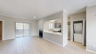 This single-floor residence is designed with a clean, contemporary aesthetic highlighted by light wood-style flooring, neutral gray walls, white crown molding, and textured ceilings throughout the main living areas. The spacious living room serves as the centerpiece of the layout, featuring a fireplace with a white mantel and a sliding glass door fitted with vertical blinds that opens to a private outdoor space, filling the room with natural light.

Adjacent to the living area, the kitchen connects via a pass-through opening with a built-in sink, creating a functional and visually open relationship between the two spaces. Inside the kitchen, gray shaker-style cabinetry pairs with white countertops and a full suite of stainless steel appliances, including a refrigerator, range, and built-in microwave. In-unit laundry is conveniently located nearby.

The dining area benefits from large windows that invite additional natural light and outdoor views. The bedrooms are finished with plush carpet, neutral walls, and windows that further enhance the sense of brightness. The bathroom features a white quartz vanity countertop, an undermount sink, a framed mirror, and modern light fixtures, contributing to the space's polished, move-in-ready character.