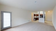 This single-floor residence features a thoughtfully designed 1-bedroom, 1-bathroom layout that makes excellent use of its space. The open living area is finished with plush, neutral-toned carpeting and crisp white walls, creating a bright and airy atmosphere that feels welcoming and versatile. Recessed ceiling vents and flush lighting fixtures contribute to the clean, streamlined aesthetic throughout.

The living area flows naturally toward the kitchen, which is defined by rich, dark wood cabinetry that provides a striking contrast to the light-colored walls and countertops. The kitchen is equipped with modern black appliances, including a refrigerator and microwave, and features a raised breakfast bar that serves as both a functional workspace and a casual dining surface. Tile flooring in the kitchen offers a practical transition from the carpeted living space.

The layout is efficiently organized, with a clear sightline from the main living area into the kitchen, enhancing the sense of openness. The neutral color palette throughout makes the space highly adaptable to a variety of interior styles. Overall, this residence combines functional design with clean, modern finishes to deliver a comfortable and inviting living environment.