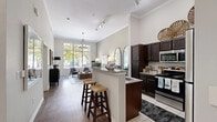 Located at 4000 Sigma Rd in Farmers Branch, TX, this thoughtfully designed one-bedroom, one-bathroom residence offers a well-appointed single-floor layout that maximizes both comfort and functionality. The open-concept kitchen and living area serves as the heart of the home, featuring soaring ceilings adorned with crown molding and track lighting. The kitchen is equipped with stainless steel appliances, rich dark-espresso cabinetry, granite countertops, a classic subway tile backsplash, and a peninsula with bar seating — ideal for casual dining or entertaining. Hardwood-style flooring flows seamlessly into the living area, where oversized windows flood the space with natural light and frame picturesque views of mature, tree-lined surroundings. The living room offers a generous, airy feel enhanced by a stylish chandelier. The spacious primary bedroom features plush carpet, tall windows with outdoor views, and direct access to the closet. The full bathroom includes tile flooring, dark vanity cabinetry, and a tub-shower combination. A dedicated hallway and closet provide practical storage. The overall ambiance is warm and refined, blending modern finishes with an inviting, well-lit atmosphere throughout.