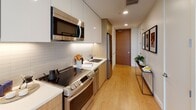 This contemporary single-floor residence offers a refined and thoughtfully designed living experience. Light hardwood flooring runs throughout, complementing a clean, modern aesthetic anchored by crisp white walls and recessed lighting.

The bedroom is a serene retreat, centered around a plush bed with neutral-toned linens and framed art above. A generous walk-in closet with built-in shelving and hanging rails provides ample storage. Floor-to-ceiling sliding glass doors open to a private balcony, flooding the room with natural light and framing sweeping panoramic views of the city skyline and distant mountains beyond.

The galley-style kitchen is efficiently designed with high-gloss white upper cabinetry, warm wood lower cabinets, a subway tile backsplash, and a full suite of stainless steel appliances including a range, over-range microwave, and refrigerator. The entry hallway doubles as a functional transition space, accented with curated art and a console table.

The bathroom features a spacious glass-enclosed walk-in shower with large-format white subway tile, a built-in niche, and taupe floor tile for a clean, spa-like atmosphere. A hallway gallery wall displaying a triptych of bold, colorful contemporary prints adds an artistic touch to the space, reinforcing the residence's stylish, urban character throughout.