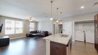 Located at 801 W 4th Ave in Stillwater, Oklahoma, this well-appointed 2-bedroom, 2-bathroom unit offers a thoughtfully designed single-level layout. The open-concept kitchen and living area serves as the heart of the home, where rich dark-cabinetry kitchen pairs with granite countertops, stainless steel appliances, and a large center island with bar seating and pendant lighting overhead. The living room features wood-style plank flooring, a ceiling fan, and multiple windows that allow natural light to fill the space. Both bedrooms are carpeted and equipped with ceiling fans. The primary bedroom offers a generous footprint with access to its own bathroom, while the second bedroom includes a window with natural light. Each bathroom is finished with wood-style flooring, a tub-shower combination, and clean, neutral tones. The second bathroom also features dark wood vanity cabinetry with a white countertop. A dedicated in-unit laundry area houses a full-size washer and dryer. Throughout the unit, neutral wall tones and consistent finishes create a cohesive and practical living environment.