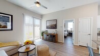 This single-story residence features a cohesive modern design unified by warm wood-look flooring, neutral gray walls, and white trim throughout. The living area is bright and welcoming, anchored by a ceiling fan overhead and a sliding glass door fitted with vertical blinds that opens to an outdoor space, allowing generous natural light to fill the room. Desert-themed artwork adds a regional character to the space.

The kitchen is well-equipped with white cabinetry, gray quartz-style countertops, stainless steel appliances including a range, microwave, dishwasher, and refrigerator, plus a central island that provides additional workspace. A large window above the sink enhances the kitchen's brightness.

The bedrooms are quietly appointed with multiple windows dressed in blinds and curtains, offering ample natural light while maintaining privacy. Each room accommodates generous storage and maintains the consistent neutral palette found throughout.

Two bathrooms serve the unit, one featuring a combined tub and shower with sliding glass doors, and another offering a walk-in shower with glass enclosure. Both include white cabinetry, dark countertops, and large mirrors, delivering a clean, contemporary aesthetic throughout.