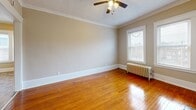 Located at 12933 Clifton Blvd in Lakewood, Ohio, this one-bedroom, one-bathroom unit offers a blend of classic architectural charm and functional layout across a single floor. The living room serves as the focal point of the space, showcasing rich hardwood floors, elegant crown molding, and a white-painted brick fireplace that adds character and warmth. Two windows allow natural light to fill the room, while a ceiling fan and cast-iron radiator provide year-round comfort. The bedroom mirrors this classic aesthetic with the same gleaming hardwood floors, crown molding, a ceiling fan, and a radiator beneath a bright window. The kitchen is efficiently designed with warm oak cabinetry, dark countertops, a white gas range, a stainless steel sink, and a clean white subway tile backsplash. Stone-look tile flooring extends through the kitchen and into the hallway, connecting to a pantry and closet for added storage. The bathroom features a full tub-shower combination with a white surround. Throughout the unit, neutral warm-toned walls and consistent trim work create a cohesive and timeless interior, reflecting the enduring character typical of Lakewood's historic residential architecture.