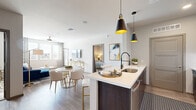 Located at 7200 N 91st Ave in Glendale, AZ, this thoughtfully designed 2-bedroom, 2-bathroom residence offers a contemporary open-concept layout across a single floor. The kitchen serves as a central hub, featuring rich dark cabinetry, stainless steel appliances including a full-size refrigerator, microwave, and gas range, along with a peninsula island with white quartz countertops and stylish pendant lighting — seamlessly connecting to the dining and living areas. The living room is bathed in natural light from a large bank of windows and includes wood-style flooring and a ceiling fan. Both bedrooms offer plush carpeting, ceiling fans, and generous windows with outdoor views. The primary bedroom connects to a well-appointed en-suite bathroom featuring a walk-in shower with white tile surround, a dark-cabinetry vanity with a white countertop, and wood-style flooring. The second bathroom mirrors this modern aesthetic. Additional highlights include a dedicated laundry area, a closet for extra storage, and a private balcony. The overall design palette of neutral tones, modern fixtures, and cohesive finishes creates a clean, contemporary living environment.