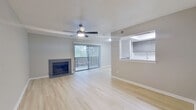 This single-floor residence offers a cohesive, modern aesthetic defined by light wood-style flooring that runs throughout the main living areas and bedroom. The open living room serves as the central hub of the space, highlighted by a tile-surround fireplace along one wall and a ceiling fan with integrated lighting overhead. A textured ceiling adds subtle visual depth, while a large sliding glass door fitted with vertical blinds fills the room with natural light and provides outdoor access.

Adjacent to the living area, the kitchen is connected via a pass-through opening that maintains an open, communicative layout. The kitchen is equipped with gray shaker-style cabinetry, white countertops, a subway tile backsplash, and stainless steel appliances including a range, over-the-range microwave, and dishwasher. A sink is visible at the pass-through, adding practicality to the design.

The bedroom features the same light flooring, neutral gray walls, and a closet, offering a clean and functional space. The bathroom is finished with a gray-tiled tub and shower surround, light wood-style flooring, a gray vanity with a white countertop, and chrome fixtures, completing the unit's consistent, contemporary palette throughout.