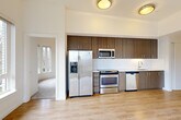Located at 1525 SW 11th Ave in Portland's vibrant SW neighborhood, this two-bedroom, two-bathroom residence offers a well-designed single-floor layout with modern finishes throughout. The open-concept kitchen and living area serves as the heart of the home, featuring light hardwood flooring, tall ceilings, and stainless steel appliances including a gas range, built-in microwave, refrigerator, and dishwasher. Rich dark wood cabinetry with a white subway tile backsplash adds a contemporary contrast. The living area opens directly onto a private balcony through glass French doors, offering views of the Portland cityscape and surrounding greenery, with a wall-mounted mini-split system providing efficient climate control. The primary bedroom is generously proportioned, showcasing a curved bay window arrangement that frames lush tree views and fills the room with natural light, complemented by plush carpeting. The second bedroom also features hardwood-style flooring, a wall-mounted AC unit, and a large window with urban views. Both bathrooms are well-appointed: one features a walk-in shower with white subway tile, a dark accent band, and a sliding glass door, while the other includes a full soaking tub and a wood-toned vanity. A clean, well-lit hallway connects all rooms seamlessly.