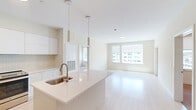 This thoughtfully designed 2-bedroom, 2-bathroom residence at 39 Trotter Road in Weymouth, MA offers a clean, contemporary aesthetic throughout. The open-concept kitchen and living area serves as the heart of the home, featuring light wood-style flooring, a sleek kitchen island with a stainless steel sink, and pendant lighting overhead. The kitchen is outfitted with flat-front white cabinetry, a herringbone tile backsplash, stainless steel appliances including a range and refrigerator, and generous counter space. The living area extends comfortably from the kitchen, bathed in natural light from large windows with roll-down shades, and includes access to an outdoor deck through a glass-panel door. Both bedrooms are carpeted and well-lit by dual windows offering exterior views, providing a calm and comfortable retreat. Three closets, including a walk-in with wire shelving, offer ample storage. The two bathrooms are finished with neutral tile flooring — one featuring a tiled tub-shower combination, and the other with a separate shower. An in-unit laundry area completes this well-appointed home, making it a highly functional and modern living space.
