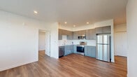 Located at 22199 NE Sandy Blvd in Fairview, Oregon, this modern 2-bedroom, 2-bathroom unit offers a well-designed single-level layout with contemporary finishes throughout. The open-concept kitchen and living area serves as the heart of the space, featuring sleek gray cabinetry, stainless steel appliances including a refrigerator, electric range, microwave, and dishwasher, along with light quartz countertops and wood-look plank flooring that extends throughout the unit. Recessed lighting illuminates the kitchen and living areas, creating a clean and bright atmosphere. Both bedrooms are comfortably sized, with the primary bedroom offering a built-in closet and access to a private balcony that provides open views of the surrounding neighborhood and tree-lined hills. Each bedroom includes a wall-mounted HVAC unit and windows with blinds that allow for ample natural light. The two bathrooms are finished with gray vanities, white quartz countertops, large mirrors, and a tub-shower combination. A dedicated utility room adds practical storage and functionality. A hallway with clean white walls connects all rooms efficiently. The private balcony completes this well-appointed unit, offering a relaxing outdoor retreat with scenic views.