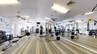 Located at 228 Dixie Dr in Tallahassee, FL, this fitness center offers a comprehensive workout facility within a single, open-plan floor. The space is designed to maximize functionality, featuring striped low-pile carpeting throughout that defines the workout areas while providing comfort underfoot. Multiple ceiling fans are suspended from the textured white ceiling, ensuring consistent airflow and a comfortable exercise environment.

The facility is well-lit by a combination of fluorescent overhead fixtures and natural light streaming in through several windows fitted with blinds, creating a bright and energizing atmosphere. A full-length wall of mirrors along one side visually expands the space and allows users to monitor their form during workouts.

The strength training area is outfitted with Cybex cable machines, a power rack with a flat bench, a comprehensive dumbbell rack with free weights, and a variety of resistance machines. The cardio section includes multiple treadmills, stair climbers, and an elliptical, catering to a wide range of fitness routines. Stability balls and additional accessories are available for functional training. A wall-mounted flat-screen television adds an element of entertainment. Direct exterior door access provides convenient entry and exit to the facility.