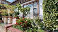 This single-story property makes a striking first impression through its meticulously curated tropical landscaping and thoughtful architectural details. The covered front entry is framed by elegant columns and warm wood-trimmed windows and doors, lending a classic yet inviting character to the façade. Lush garden beds surround the entryway, filled with sago palms, cycads, colorful crotons, bromeliads, and flowering impatiens, all set against a backdrop of smooth river rock ground cover that adds a polished, low-maintenance aesthetic.

A paved brick walkway winds along the side of the property, bordered by an abundance of tropical plantings including towering palms, bird-of-paradise, and banana trees that cast dappled shade across the path. Vibrant blooms in reds, whites, and pinks add seasonal color throughout the landscape, while large decorative ceramic urns and ornamental sculptures serve as eye-catching focal points.

Adding a distinctive artistic touch, colorful mosaic wall panels are mounted near one of the building's entrances, complemented by a stylish wall sconce and clean stone-clad exterior walls. The overall ambiance of this property is that of a tropical retreat — verdant, well-maintained, and rich in visual detail, offering a serene and welcoming environment from every angle.