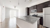 This single-floor residence combines contemporary finishes with a functional, open layout. The kitchen serves as a central highlight, showcasing a large granite-topped island with an integrated sink and pendant lighting overhead. Dark espresso cabinetry extends from floor to ceiling, providing generous storage, while stainless steel appliances — including a refrigerator, electric range, and over-the-range microwave — contribute a sleek, modern aesthetic. Wood-look flooring runs throughout the main living areas, reflecting natural light and adding warmth to the neutral white and gray color palette.

The living area is bright and open, featuring a ceiling fan and a sliding door fitted with vertical blinds that allow for controlled natural light. The seamless flow between the kitchen and living space creates an inviting, versatile environment suitable for both everyday living and entertaining.

The bedrooms are finished with plush wall-to-wall carpeting and feature windows with horizontal blinds, providing comfort and privacy. The bathroom is well-appointed with dark vanity cabinetry topped with a granite countertop, a tub-shower combination with clean white tile surround, and wood-look flooring that ties cohesively to the rest of the unit.