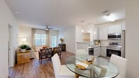 Located at 40 Cohen Walker Dr in Warner Robins, GA, this single-story home offers a thoughtfully designed open-concept layout across two bedrooms and two bathrooms. The living room is bright and welcoming, featuring wood-look flooring, a ceiling fan, and large windows dressed with elegant floor-to-ceiling drapes that invite generous natural light. The space flows seamlessly into the dining area, where a glass-top round table sits adjacent to the kitchen. The kitchen is well-equipped with crisp white shaker cabinets, granite-style countertops, stainless steel appliances including a range, microwave, dishwasher, and refrigerator, all set on light hardwood-style flooring. The primary bedroom is a comfortable retreat with warm neutral tones and wood-look flooring, accompanied by a spacious walk-in closet outfitted with wire shelving systems. The bathrooms are clean and functional, featuring granite-top vanities and a walk-in shower with chrome fixtures. Two closets provide ample storage throughout. The attached garage is a standout feature, offering generous space with direct interior access. The home's consistent use of neutral tones, modern finishes, and cohesive flooring throughout creates a polished and comfortable living environment.