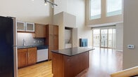 Located in Saint Paul, MN, this two-story, two-bedroom, one-bathroom residence offers a well-designed layout across two floors. The main level is anchored by a dramatic open-concept kitchen and living area with soaring double-height ceilings that flood the space with natural light from tall clerestory windows. The kitchen is thoughtfully appointed with rich warm-toned cabinetry, dark granite countertops, a large center island, stainless steel appliances including a refrigerator, range, microwave, and dishwasher, plus a tiled backsplash and hardwood flooring. A stacked in-unit washer and dryer is conveniently tucked within a dedicated enclosure. The living room showcases a sleek modern fireplace, continued hardwood flooring, and floor-to-ceiling sliding glass doors opening to a balcony with urban views. A wood staircase connects the floors. The upper level hosts two carpeted bedrooms, each with large windows offering outdoor views. The primary bedroom provides direct access to the full bathroom, which features tile flooring, a soaking tub with shower, and warm wood vanity cabinetry. A dedicated closet completes the upper level. The space blends contemporary urban design with functional, comfortable living throughout.