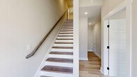 Located at 442 Centre St in Pleasant View, TN, this three-story townhome offers a well-organized layout across three distinct levels. The ground floor features an attached garage with a clean, neutral-toned interior and direct interior access via a staircase leading to the upper levels. The main living floor serves as the heart of the home, hosting an open-concept kitchen and living area. The kitchen is appointed with crisp white shaker cabinetry, a herringbone tile backsplash, stainless steel appliances, light wood-tone flooring, and a two-toned island with an undermount sink and pendant lighting. A pantry and half bath round out this level's functionality. The top floor is dedicated to all three bedrooms, including a generously sized primary suite with a walk-in closet, light wood flooring, and a ceiling fan. Secondary bedrooms feature plush carpet, ample closet space, and clean neutral walls. The four bathrooms are finished with white vanities, wood-look tile flooring, and combination tub/shower units. A private balcony off the upper level offers open outdoor views of the surrounding Pleasant View neighborhood under wide Tennessee skies. The exterior presents a modern brick and siding facade with manicured landscaping and a welcoming streetside presence.