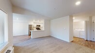 This single-floor residence is designed with a clean, modern aesthetic throughout. The open-concept living and dining area features neutral-toned carpet and flows directly into the kitchen, which is defined by a peninsula countertop that doubles as a breakfast bar. The kitchen is equipped with stainless steel appliances—including a refrigerator, range, and microwave—complemented by white shaker cabinetry, light countertops, and wood-look flooring. Recessed lighting illuminates the space efficiently.

The living area benefits from multiple windows offering views of mature trees, and a door provides access to an outdoor balcony, allowing natural light to fill the interior. A dedicated laundry area with a full-size washer and dryer is conveniently accessible from the main living space.

The bedroom is generously proportioned with soft carpet, a reach-in closet with built-in shelving, and a window overlooking the outdoors. Two bathrooms serve the unit: one features a white vanity with a wide mirror and tile flooring, while the second includes a full tub-shower combination with brushed nickel fixtures and matching tile floors. The overall palette of whites and neutrals creates a bright, cohesive atmosphere throughout.