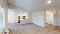 This single-floor residence is designed with a clean, modern aesthetic throughout. The open-concept living and dining area features neutral-toned carpet and flows directly into the kitchen, which is defined by a peninsula countertop that doubles as a breakfast bar. The kitchen is equipped with stainless steel appliances—including a refrigerator, range, and microwave—complemented by white shaker cabinetry, light countertops, and wood-look flooring. Recessed lighting illuminates the space efficiently.

The living area benefits from multiple windows offering views of mature trees, and a door provides access to an outdoor balcony, allowing natural light to fill the interior. A dedicated laundry area with a full-size washer and dryer is conveniently accessible from the main living space.

The bedroom is generously proportioned with soft carpet, a reach-in closet with built-in shelving, and a window overlooking the outdoors. Two bathrooms serve the unit: one features a white vanity with a wide mirror and tile flooring, while the second includes a full tub-shower combination with brushed nickel fixtures and matching tile floors. The overall palette of whites and neutrals creates a bright, cohesive atmosphere throughout.