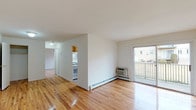 This two-floor residence at Carteret Gardens is designed with a clean, functional layout spread across two distinct levels. The main floor centers around a spacious, open living area finished with polished hardwood flooring that extends throughout. Bright white walls and natural light from a large sliding glass door create an airy atmosphere, with the door opening directly onto a private balcony offering outdoor views. A wall-unit air conditioner and baseboard heating provide year-round climate control.

The kitchen is efficiently arranged with warm wood cabinetry, granite countertops, a stainless steel sink, a dishwasher, and a gas range with an adjacent refrigerator. A window above the counter brings in additional natural light. The bathroom features tile flooring, a wood-vanity with a white countertop, and a tub-shower combination enclosed by sliding glass doors.

Bedrooms are well-proportioned, each with hardwood floors, baseboard heating, and generous natural light. One bedroom notably includes two side-by-side closets, offering substantial storage capacity.

The lower level provides a sizable bonus space with painted flooring, a baseboard heating system, and a window, connected to the main floor via an open staircase with a metal railing—suitable for use as additional living, storage, or flex space.