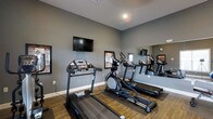 Located at 2753 Michaelsway Ave in Lancaster, Ohio, this single-floor fitness center is designed to provide residents with a convenient and functional workout space. The room features a clean, modern aesthetic with smooth gray walls and durable hardwood-style flooring that adds warmth to the space. Cardio equipment, including treadmills and an elliptical machine, is thoughtfully arranged to maximize the available floor space and allow for comfortable use. A wall-mounted flat-screen television is positioned at eye level, offering entertainment during workouts. A large mirror spans one wall, visually expanding the room and allowing users to monitor their form while exercising. Framed informational displays are mounted on the walls, contributing to the motivating atmosphere. Recessed lighting provides bright, even illumination throughout the space. A wall clock near the mirror helps users keep track of their workout time. The overall ambiance is practical and inviting, with a well-maintained environment that supports an active lifestyle.