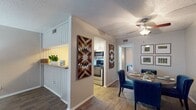 This single-floor residence showcases a harmonious blend of modern and rustic elements. The open-concept layout seamlessly connects the kitchen and dining areas, creating a spacious feel. The kitchen boasts stainless steel appliances and a convenient breakfast bar, while the dining space accommodates a table for shared meals. Hardwood flooring runs throughout, adding warmth to the neutral color palette. Distinctive wooden wall art pieces with geometric patterns serve as striking focal points, infusing character into the space. Ceiling fans and recessed lighting enhance comfort and ambiance. The overall design balances functionality with aesthetic appeal, resulting in a welcoming and stylish home environment.