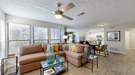 This single-floor residence offers a thoughtfully designed open-concept layout that seamlessly connects the living, dining, and kitchen areas. The living room is generously sized, anchored by a large sectional sofa and a ceiling fan with light fixture overhead. Multiple windows fitted with horizontal blinds allow abundant natural light to fill the space, while light wood-style flooring extends throughout the common areas, lending a warm, cohesive aesthetic.

The kitchen is well-equipped with white shaker cabinetry, granite countertops, a subway tile backsplash, and a full suite of stainless steel appliances including a gas range, dishwasher, microwave, and refrigerator. A breakfast bar with bar seating connects the kitchen to the dining area, which comfortably accommodates a full dining table. A dedicated storage closet with louvered bifold doors is conveniently located nearby.

The bedrooms feature plush carpeting, ceiling fans, ample closet space, and windows that provide natural light and outdoor views. The bathroom includes a granite vanity, wood-style flooring, and a tub-shower combination. A dedicated laundry closet houses a full-size washer and dryer, adding everyday convenience to this well-rounded residence.