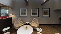 Located at 733 15th St NW in the heart of Washington, DC, this single-floor commercial space offers a polished and functional environment well-suited for gatherings, meetings, or events. The entry area makes a strong first impression, featuring a grand staircase with ornate metal railings, an accessibility lift, and natural light streaming in through Roman shade-dressed windows that overlook the surrounding streetscape.

The fully equipped kitchen is a standout feature, outfitted with rich dark-wood cabinetry, dark granite countertops, a stainless steel full-size refrigerator, microwave, and a double-basin sink. Durable tile flooring anchors this workspace, which is designed for practical, high-volume use. Adjacent to the kitchen, a wraparound bar counter with a granite surface and built-in sink is lined with sleek, modern bar stools — ideal for casual dining or catering service.

The lounge area exudes a contemporary sophistication, furnished with tufted cream leather accent chairs, round white side and coffee tables, and textured carpet underfoot. Three framed landscape artworks hang prominently on the wall, adding a refined, curated aesthetic. Recessed lighting and exposed ceiling beams lend architectural character throughout the space, contributing to an atmosphere that is both professional and inviting.
