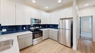 This three-floor home in Perrysburg, Ohio offers a well-organized layout designed for comfortable living. The main level serves as the heart of the home, featuring an open-concept kitchen and living room with soaring vaulted ceilings, abundant natural light from multiple windows, and light-toned hardwood-style flooring throughout. The kitchen is outfitted with white shaker-style cabinetry, granite countertops, stainless steel appliances, and a striking deep-blue tile backsplash. A pendant light fixture and balcony access add character and functionality to this central gathering space. Carpeted staircases with white railings connect all three levels. The upper floor hosts the bedrooms, including a generously sized primary suite with a walk-in closet featuring wire shelving, as well as additional bedrooms with plush carpet and clean, neutral walls. The bathrooms are finished with granite-topped vanities and tub/shower combinations with light wood-style flooring. A versatile loft space on the upper level offers flexible use under a sloped ceiling. A dedicated laundry room with a full-size washer and dryer completes the home's practical offerings. Two closets provide ample storage throughout.