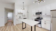 Located at 2656 Creekwood Cir in Moraine, Ohio, this single-floor residence showcases a thoughtfully updated interior with a clean, modern aesthetic throughout. The kitchen serves as the standout space, featuring white shaker-style cabinetry extending to the ceiling, a classic white subway tile backsplash, and a full suite of stainless steel appliances including a range, over-the-range microwave, dishwasher, and refrigerator. Light wood-look flooring runs through the kitchen and dining area, complementing the bright, white walls and adding warmth to the space. A striking mid-century modern sputnik chandelier with gold accents serves as a focal point, lending a stylish contrast to the crisp white palette. A white-topped dining table with dark metal legs anchors the open dining area adjacent to the kitchen.

The bedrooms are finished with neutral carpet and feature textured ceilings, while windows with horizontal blinds bring in natural light and outdoor views. The bathroom is outfitted with a tiled tub-and-shower combination, matte black fixtures and hardware, a dark-framed vanity with a white countertop, and light wood-look flooring that ties cohesively to the rest of the unit. Overall, the space presents a fresh, contemporary feel throughout.