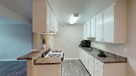 This single-story unit offers a practical and well-organized layout across several distinct spaces. The galley-style kitchen is efficiently designed with white cabinetry lining both walls, providing ample upper and lower storage. Granite-style laminate countertops, a double-basin sink, a gas range with overhead ventilation, and wood-look vinyl flooring complete the functional cooking space.

A pass-through window connects the kitchen to the adjoining living and dining area, enhancing the sense of openness between spaces. The living area features warm wood-look flooring, a ceiling fan with light fixture, and a textured ceiling. A sliding glass door leads directly to a private outdoor patio, allowing natural light to fill the room.

The bedroom is carpeted and features neutral-toned walls, a textured ceiling, and a window fitted with vertical blinds that provide both privacy and natural light.

The bathroom includes a full-size soaking tub and shower combination with a curtain rod, wood-look vinyl flooring, and a vanity with stone-style countertops. Neutral wall tones throughout the unit create a cohesive, clean aesthetic that contributes to the space's overall calm and functional ambiance.