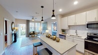 Located at 728 N Church St in Spartanburg, South Carolina, this thoughtfully designed single-floor residence offers a bright, open-concept layout with contemporary finishes throughout. The kitchen serves as a central hub of the home, featuring white shaker-style cabinetry, a classic subway tile backsplash, quartz countertops, stainless steel appliances, and a spacious island with bar seating illuminated by striking pendant lighting. The kitchen flows seamlessly into the living area, which benefits from large windows that invite abundant natural light and provide outdoor views, complemented by a ceiling fan overhead and access to a private balcony. The two bedrooms are generously sized with plush carpeting, large windows, and ceiling fans, creating comfortable, well-lit retreats. The primary bathroom offers a glass-enclosed shower with large-format tile, while the secondary bathroom features a soaking tub with decorative tile surround and a single vanity with ample cabinet storage. Both bathrooms include wood-look flooring that lends warmth to the neutral palette. A dedicated in-unit laundry area houses a full-size washer and dryer. Throughout, the residence maintains a cohesive, modern aesthetic with light walls, wood-look flooring in the main living areas, and consistent contemporary hardware and fixtures.