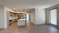 Located near US-101 in Camarillo, California, this single-story unit presents a contemporary design with a clean, neutral palette throughout. The open-concept layout connects the kitchen and living area seamlessly, creating a bright and functional shared space. Wood-look luxury vinyl plank flooring runs through the main living areas, complementing the modern aesthetic.

The kitchen is well-appointed with wood-grain cabinetry, white quartz countertops, and a full suite of stainless steel appliances including a gas range, microwave, dishwasher, and refrigerator. A central island with a white countertop provides additional prep space and casual seating. Pendant lighting and recessed fixtures illuminate the area effectively.

The living room is generously sized, featuring large windows that invite natural light and offer views of the surrounding landscape. Bedrooms are finished with plush carpeting and benefit from good natural light. The primary bedroom includes access to a spacious walk-in closet outfitted with multi-tier shelving and hanging rods. Bathrooms feature tile surround tub-shower combinations, light wood-look flooring, built-in shelving, and chrome fixtures throughout.