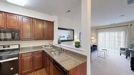 Located at 900 Grand Central Dr in Hamilton, NJ, this well-appointed one-bedroom, two-bathroom residence offers a thoughtfully designed single-level layout. The kitchen is a standout feature, showcasing rich cherry wood cabinetry, granite countertops, hardwood flooring, and stainless steel appliances including a gas range and built-in microwave. A pass-through window connects the kitchen to the living area, enhancing the open-concept feel. The living room is bright and inviting, with plush carpeting, neutral tones, and a sliding glass door with vertical blinds that floods the space with natural light and provides access to an outdoor area. The spacious primary bedroom offers generous proportions, soft carpeting, a large walk-in closet with built-in shelving, and a dedicated en-suite bathroom. A second full bathroom serves guests, featuring tile flooring, a tub-shower combination with tiled surround, and warm wood vanity cabinetry. Both bathrooms maintain a clean, classic aesthetic with white fixtures and ample vanity space. Throughout the residence, a cohesive neutral palette and consistent finishes create a calm, comfortable ambiance suited for everyday living.