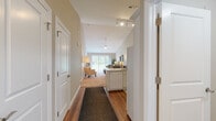 This thoughtfully designed single-floor residence offers a cohesive layout that balances comfort and functionality. A welcoming entryway hallway with rich hardwood flooring and track lighting leads into the heart of the home, where the kitchen and living areas flow seamlessly together. The kitchen is outfitted with white cabinetry, light stone countertops, a full suite of white appliances including a refrigerator, range, microwave, and dishwasher, and continues the warm hardwood flooring underfoot. The open living room features vaulted ceilings, a ceiling fan, and a large window that frames outdoor greenery, filling the space with natural light. Neutral walls and plush carpeting create a relaxed, inviting atmosphere. The dedicated office is a bright, carpeted room with windows on two walls, providing ample natural light — ideal for focused work or study. The bedroom is generously proportioned with soft carpet, multiple windows overlooking lush trees, and convenient access to additional spaces. The full bathroom features a tub-shower combination, white vanity, and durable hardwood-style flooring. Completing the residence is an in-unit laundry area with a full-size washer and dryer, adding everyday convenience to this well-rounded home.