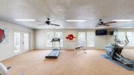 Located at 922 N Sidney Ave in Russellville, Arkansas, this dedicated exercise room offers a generously sized, single-floor fitness space designed to support a well-rounded workout regimen. The room is carpeted throughout and finished with a textured ceiling, lending it a clean and functional aesthetic.

Natural light floods the space through multiple windows along the walls, complemented by recessed fluorescent lighting panels that ensure bright, even illumination at any hour. Two ceiling fans are positioned throughout the room to maintain comfortable airflow during workouts.

The fitness area is thoughtfully equipped with a variety of cardio machines, including a treadmill, a stationary recumbent bike, and an elliptical trainer. A dedicated strength-training zone features a multi-position weight bench and a full dumbbell rack with a range of weights, catering to both beginners and experienced fitness enthusiasts. A large wall mirror along one side of the room enhances the sense of space and allows for proper form checks during exercise.

French doors and additional entry points provide convenient access, while an emergency exit ensures safety compliance. Decorative Arkansas Razorbacks artwork adds a spirited, local touch to the walls. The open floor plan allows equipment to be arranged with ample room to move freely, making this a practical and inviting fitness environment.