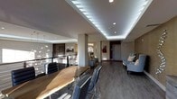 This contemporary space showcases a thoughtfully designed open-concept layout that blends modern aesthetics with practical functionality. The interior is anchored by a striking live-edge wood dining table surrounded by sleek black chairs, serving as a natural focal point that balances organic warmth with modern design sensibilities.

The ceiling is a standout architectural feature, incorporating a recessed tray design lined with continuous LED strip lighting that casts a soft, ambient glow throughout the space. Recessed pot lights provide additional illumination, ensuring the area is well-lit from multiple angles. A sculptural, cascading pendant light fixture adds an artistic touch, enhancing the upscale atmosphere.

Wide-plank hardwood flooring in a rich grey-toned finish runs throughout, complementing the neutral colour palette of the walls and contributing to a cohesive, modern feel. A metal railing with horizontal balusters defines a mezzanine or overlook area, adding depth and visual interest to the layout.

Seating areas furnished with contemporary grey upholstered chairs are positioned thoughtfully around the space, offering comfortable lounge zones. Structural columns are integrated seamlessly into the design, reinforcing the open yet well-defined nature of the floor plan. Overall, the space exudes a polished, upscale ambiance suited for both social gatherings and everyday use.