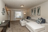 This two-floor residence offers a well-organized layout that balances comfort and functionality throughout. The main level showcases an open-concept design where the living room, dining area, and kitchen flow seamlessly together. The living room features plush carpeting, a textured ceiling, and a large window with decorative curtains that allow natural light to fill the space. Adjacent to the living area, the dining space is anchored by a pendant chandelier and benefits from vaulted ceilings that lend an airy, open feel. A decorative arched accent window adds architectural character to this area. The kitchen is outfitted with warm wood cabinetry, dark countertops, and black appliances including a range, microwave, and refrigerator, all set atop durable wood-look flooring. A bathroom on the main level features a vanity with rich wood cabinetry and a light countertop. The upper level hosts carpeted bedrooms with vaulted ceiling details and windows offering natural light. A full bathroom on this level includes a tub-shower combination with tile flooring. Throughout, the space maintains a warm, neutral palette with consistent trim details that create a cohesive and inviting atmosphere across both floors.