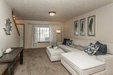 This two-floor residence offers a well-organized layout that balances comfort and functionality throughout. The main level showcases an open-concept design where the living room, dining area, and kitchen flow seamlessly together. The living room features plush carpeting, a textured ceiling, and a large window with decorative curtains that allow natural light to fill the space. Adjacent to the living area, the dining space is anchored by a pendant chandelier and benefits from vaulted ceilings that lend an airy, open feel. A decorative arched accent window adds architectural character to this area. The kitchen is outfitted with warm wood cabinetry, dark countertops, and black appliances including a range, microwave, and refrigerator, all set atop durable wood-look flooring. A bathroom on the main level features a vanity with rich wood cabinetry and a light countertop. The upper level hosts carpeted bedrooms with vaulted ceiling details and windows offering natural light. A full bathroom on this level includes a tub-shower combination with tile flooring. Throughout, the space maintains a warm, neutral palette with consistent trim details that create a cohesive and inviting atmosphere across both floors.