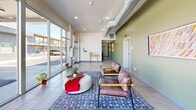 Located at 609 S Thornton Ave in Dalton, Georgia, this contemporary single-story commercial space offers a thoughtfully designed interior that balances functionality with modern aesthetics. The open floor plan is anchored by a welcoming lounge area near the entrance, where large floor-to-ceiling glass windows flood the space with natural light and provide sweeping views of the surrounding streetscape. Comfortable seating, a plush area rug, and curated artwork on sage-green accent walls create an inviting, professional atmosphere throughout.

Exposed spiral ductwork runs along the ceiling, lending an industrial-chic character that complements the clean, light-tiled flooring found throughout the space. A dedicated conference room features a generous wooden meeting table with ample seating, natural light from surrounding windows, and views of the outdoors—ideal for collaborative work sessions. A glassed corner nook provides an intimate workspace bathed in panoramic natural light, perfect for focused tasks or smaller meetings.

A private office or utility room is accessible via the main corridor, which is lined with tasteful artwork and continues the cohesive green-and-white color palette. Recessed lighting and modern fixtures add a polished finish, making this space well-suited for a variety of professional or creative uses.