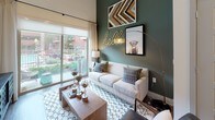 This single-floor residence showcases a thoughtfully designed layout with contemporary finishes throughout. The kitchen is a standout feature, boasting dark espresso cabinetry that extends to impressive heights, stainless steel appliances including a refrigerator, range, microwave, and dishwasher, and crisp white countertops. A center island with pendant lighting above adds both function and style, while wood-look flooring grounds the space with warmth. Built-in wall niches near the entryway provide a charming display area.

The open living room is anchored by soaring ceilings and a bold accent wall, creating a dramatic yet inviting atmosphere. Large sliding glass doors flood the space with natural light and provide direct access to an outdoor patio with pool views beyond.

The primary bedroom features a striking full-height upholstered headboard wall and large windows dressed with blinds and sheer curtains. A second bedroom offers a bright, airy feel with ample natural light and soft carpeting. The full bathroom includes a tiled soaking tub and shower combination, dark vanity cabinetry with white countertops, and tile flooring. Direct access from the bathroom leads into a spacious walk-in closet with built-in shelving and hanging storage.