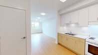 Located at 4277 Norland Ave in Burnaby, BC, this one-bedroom, one-bathroom unit offers a clean, minimalist design across a single floor. Light wood laminate flooring runs throughout the living areas and bedroom, contributing to a bright and cohesive aesthetic.

The kitchen is well-appointed with an L-shaped layout featuring light wood lower cabinetry and crisp white upper cabinets that extend to the ceiling, maximizing storage. A white coil-top range, integrated range hood, full-size refrigerator, and a stainless steel sink complete the functional space, all set against white countertops and a clean white backsplash. A flush ceiling light fixture provides ample illumination.

The bedroom is a comfortable, well-proportioned room with white walls and a large window that frames scenic views of the surrounding neighbourhood and distant mountains, allowing for generous natural light. A closet with sliding doors provides practical storage.

The bathroom is thoughtfully designed with accessibility in mind, featuring sturdy grab bars beside the bathtub-shower combination, a toilet, and a vanity with drawers and an integrated sink. Neutral flooring and white walls create a clean, functional environment.

Overall, the unit presents a bright, practical living space with a consistent neutral palette, light wood flooring, and functional layouts throughout each room.
