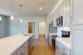 Located in La Plata, Maryland, this well-appointed 3-bedroom, 3-bathroom residence offers a thoughtfully designed single-level layout with generous living space throughout. The open-concept living, dining, and kitchen area serves as the heart of the home, featuring warm hardwood-style flooring that flows seamlessly through the main living areas. The modern kitchen is a standout, showcasing gray shaker-style cabinetry with brushed gold hardware, crisp white quartz countertops, a subway tile backsplash, a large center island with an undermount sink, pendant lighting, and a full suite of stainless steel appliances. A wide hallway connects the main living area to the three well-sized bedrooms, each carpeted for comfort. The primary bedroom includes a spacious walk-in closet outfitted with wire shelving systems. The bathrooms are finished with light wood-tone flooring, gray vanities, and clean white subway tile tub surrounds. French doors in the living area open to a private balcony, allowing natural light to pour in. A dedicated in-unit laundry room houses a full-size washer and dryer with overhead shelving. Four closets throughout the home provide ample storage, rounding out this move-in-ready residence.
