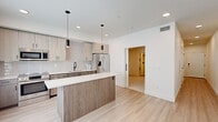 Located at 146 S Wayfinder Ave in Meridian, Idaho, this single-floor residence showcases a thoughtfully designed, contemporary interior with clean lines and a cohesive neutral palette throughout. The open-concept kitchen serves as the centerpiece of the living space, featuring light wood cabinetry, a full suite of stainless steel appliances — including a French door refrigerator, electric range, built-in microwave, and dishwasher — and a sleek white quartz countertop. A substantial kitchen island with a warm wood-toned base provides additional workspace and casual seating, while matte black pendant lights overhead add a refined, modern accent. Vertical subway tile forms an elegant backsplash along the kitchen wall, complementing the light hardwood-style flooring that flows throughout the main living areas. The bathroom continues the modern aesthetic with a wide vanity, white quartz countertop, a large backlit mirror, and matte black fixtures that echo the design language found throughout the unit. A separate room features soft carpet flooring and a sleek matte black sliding barn door, offering a versatile and stylish space. Recessed lighting throughout ensures a bright, well-illuminated environment, while crisp white walls contribute to the overall sense of openness and light.
