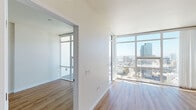 Located at 1150 E Street in San Diego's vibrant East Village neighborhood (92101), this high-rise residence offers a bright, contemporary living experience defined by clean lines and abundant natural light. Floor-to-ceiling windows frame sweeping panoramic views of the San Diego skyline and surrounding cityscape, filling the open living areas with sunlight throughout the day. Light-toned hardwood flooring runs seamlessly throughout the unit, complementing the crisp white walls and modern aesthetic. The kitchen is well-appointed with light wood cabinetry, stainless steel appliances including a French door refrigerator, electric range, and over-the-range microwave, complemented by a subway tile backsplash and a white quartz island that provides additional prep and seating space. A stacked in-unit washer and dryer adds everyday convenience. The living and sleeping areas each benefit from direct access to the floor-to-ceiling glazing, offering unobstructed city views and an airy, elevated atmosphere. The private balcony extends the living space outdoors, delivering breathtaking elevated views of the San Diego urban landscape under the Southern California sun. The overall ambiance is modern, minimalist, and light-filled, ideal for those seeking a polished urban lifestyle in the heart of downtown San Diego.