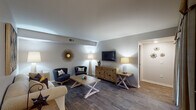 This thoughtfully designed single-floor residence offers a cohesive layout that balances comfort and functionality throughout. The living room serves as the heart of the home, featuring rich dark hardwood-style flooring, neutral gray walls, and a distinctive stepped ceiling detail. The space is generously proportioned, accommodating a full seating arrangement alongside a media console, and is accented with decorative wall art that adds warmth and personality.

Adjacent to the living area, the kitchen is outfitted with rich cherry wood cabinetry, stainless steel appliances including a refrigerator, microwave, and range, as well as a wraparound peninsula with countertop seating. Light tile flooring complements the warm wood tones throughout. The separate dining area features a ceiling fan, a large window with garden views, and hardwood-style flooring that continues from the living room.

The two bedrooms are well-sized and bright, each offering large windows that invite natural light and views of lush greenery. Both rooms feature dark hardwood-style floors. One bedroom includes a floor-to-ceiling mirrored sliding closet. The expansive bathroom includes a long dual-sink vanity with ample counter space, mirrored storage, and a separate water closet. A dedicated in-unit laundry room with side-by-side washer and dryer and built-in shelving rounds out this well-equipped residence.