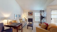 This single-floor residence offers a thoughtfully designed layout that balances comfort and functionality throughout. The living room is a standout space, featuring dramatic vaulted ceilings that lend an airy, open feel, soft carpeting, and a classic fireplace framed by a clean white mantel. Natural light pours in through shuttered windows, creating a warm and inviting atmosphere.

The kitchen is equipped with warm oak cabinetry, a double-basin stainless steel sink, stainless steel appliances including a refrigerator and dishwasher, and hardwood flooring. A peninsula with bar-height seating connects the kitchen to the main living area, making it ideal for casual dining or entertaining. The adjoining dining area features a pendant light overhead and sliding glass doors that open onto a private balcony, bringing in additional natural light and outdoor access.

The bedrooms are comfortably sized, each with plush carpeting, ceiling fans, and shuttered windows that allow for adjustable light control. The bathroom is finished with tile flooring, a combined tub and shower, and a vanity with warm wood cabinetry. Throughout the residence, a neutral color palette and consistent finishes create a cohesive and welcoming ambiance.