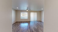 Located at 8855 N Casa Grande Hwy in Marana, Arizona, this single-story unit offers a well-designed, open-concept floor plan with a cohesive blend of modern finishes throughout. The main living area is anchored by durable wood-style plank flooring that extends through the open layout, recessed lighting, and a ceiling fan, while a large window and sliding glass door with vertical blinds allow generous natural light and outdoor access.

The kitchen is a standout feature, showcasing dark wood-grain cabinetry with sleek bar-pull hardware, white quartz-style countertops, a neutral tile backsplash, and black appliances including a range, microwave, and dishwasher. A peninsula with pendant lighting connects the kitchen to the main living space, creating an ideal flow for everyday living.

The bedrooms feature plush wall-to-wall carpeting, ceiling fans, and windows with blinds that invite natural light. The bathrooms are finished with dark vanity cabinetry, white countertops, wood-style flooring, and well-lit mirrors. One bathroom includes a full tub/shower combination. In-unit laundry hookups are also visible, adding practical convenience. The overall aesthetic is clean, contemporary, and move-in ready.