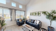 Located at 1805 Loftway Cir in Orlando, FL, this two-story home offers four bedrooms and four bathrooms across two well-proportioned floors. The main level provides the larger share of the living space and opens with a welcoming entrance that flows into a combined living, dining, and kitchen area. The living room stands out with dramatically high ceilings and large windows that allow generous natural light to pour in, complemented by elevated clerestory windows that enhance the airy, open ambiance. Light wood-look flooring runs throughout the main level, adding warmth and continuity. The galley-style kitchen features white cabinetry, gray countertops, a subway tile backsplash, and stainless steel appliances, offering an efficient and clean workspace. The bathrooms are finished with white tile surrounds, tub-shower combinations, and vanities with gray countertops. Bedrooms are carpeted and include ceiling fans and closets with wire shelving systems, offering functional storage. The upper floor houses a loft space adaptable for a home office or lounge, along with additional bedrooms. A dedicated laundry room and utility room add everyday convenience. The home's clean, neutral palette and modern finishes create a bright, cohesive living environment throughout.
