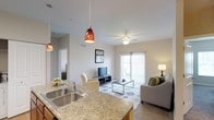 This single-floor residence offers a thoughtfully designed open-concept layout that connects the kitchen and living areas in a seamless, functional flow. The kitchen features granite countertops, a stainless steel double-basin sink, and stylish pendant lighting with rich amber glass shades that add a warm, decorative touch. The kitchen bar counter extends naturally into the living space, making it ideal for both casual dining and entertaining.

The living area is generously proportioned and bathed in natural light, courtesy of a large sliding glass door fitted with vertical blinds that leads to an outdoor area. A ceiling fan with integrated lighting anchors the center of the room, promoting airflow and comfort. Neutral-toned walls and tile flooring provide a clean, versatile backdrop throughout the space.

The living room is well-suited for relaxing and entertaining, with ample room for a full seating arrangement centered around a sleek media console. The overall ambiance is bright, airy, and contemporary, with consistent finishes and warm accent lighting that contribute to a welcoming atmosphere. A hallway visible from the main living area suggests additional private rooms beyond, completing this well-rounded single-floor layout.