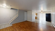 This two-story residence offers a practical and well-organized layout across both floors. The main level welcomes you through a front entry door with an arched transom window, opening into a spacious living area finished with warm hardwood flooring. A staircase with a white railing runs along one wall, leading to the upper level. The living space flows openly into a dining area, which transitions to light-colored tile flooring and is equipped with a ceiling fan and light fixture. Vertical blinds on large windows allow for adjustable natural light throughout. A baseboard heating system and a wall-mounted air conditioning unit provide year-round climate control.

The kitchen is efficiently designed with warm wood cabinetry, granite-patterned countertops, a stainless steel sink, and tile flooring. It is equipped with a black electric range, over-the-range microwave, and a black refrigerator.

Upstairs, the bedrooms are carpeted in neutral tones and feature soft gray walls, providing a calm and comfortable atmosphere. The upper hallway connects the rooms, with access panels and closet doors visible throughout. The overall aesthetic is clean and neutral, offering a functional canvas well-suited for a variety of living arrangements.
